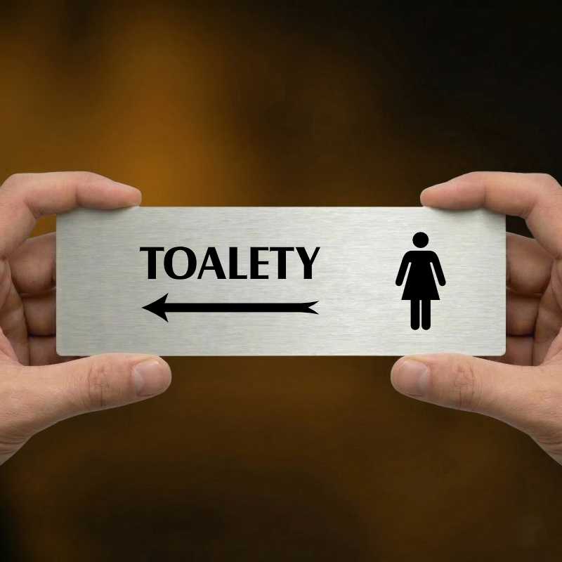 Toalety vlevo ženy, 240x79mm, zlatá popiska s okrasným rámečkem  
